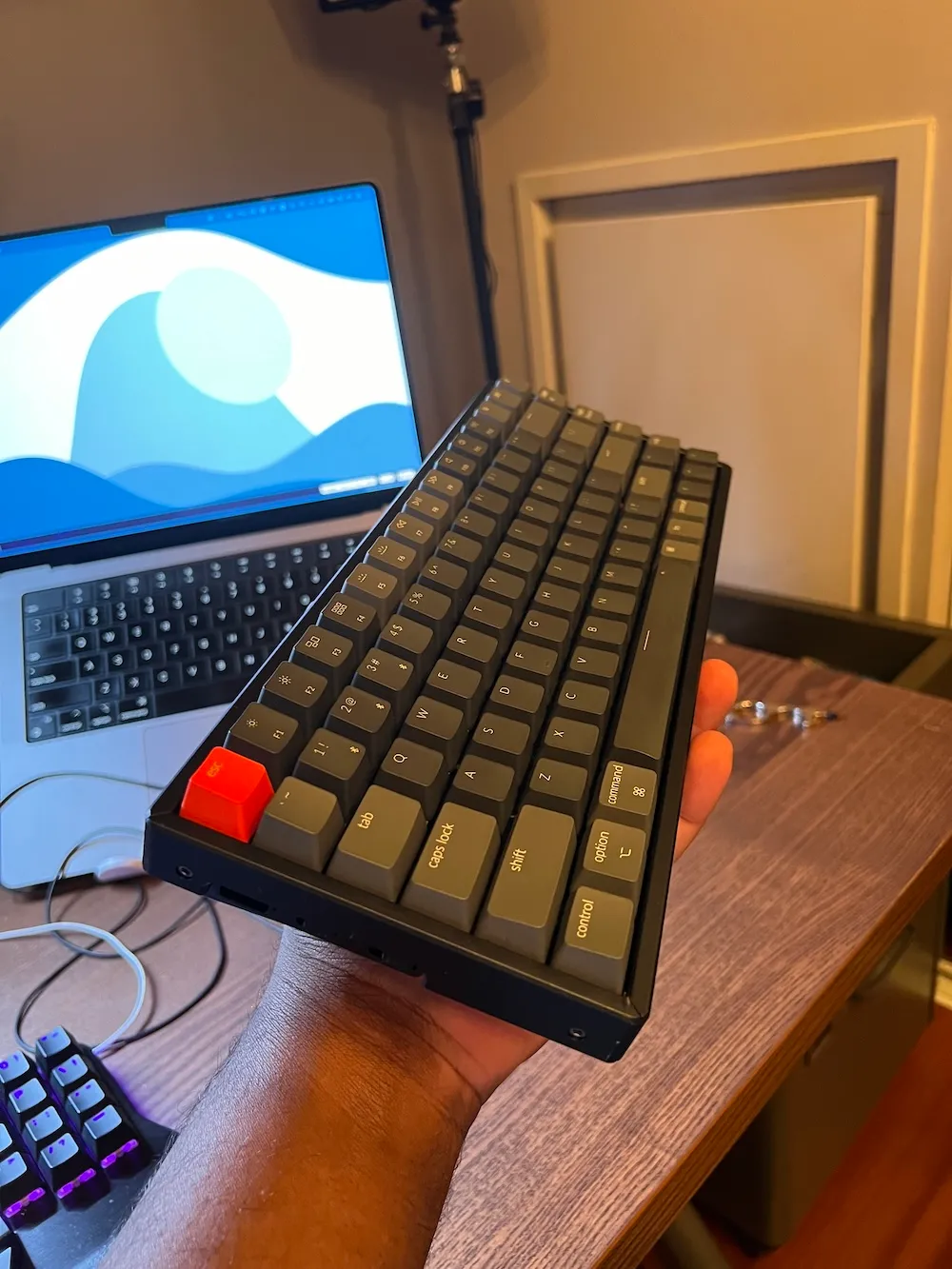 Photo of the Keychron K2 side view, in my hand, facing my MacBook Pro