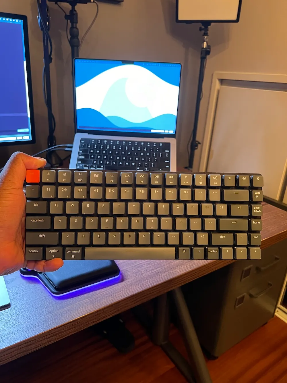 Photo of the Keychron K6 in my hand in front of my MacBook Pro